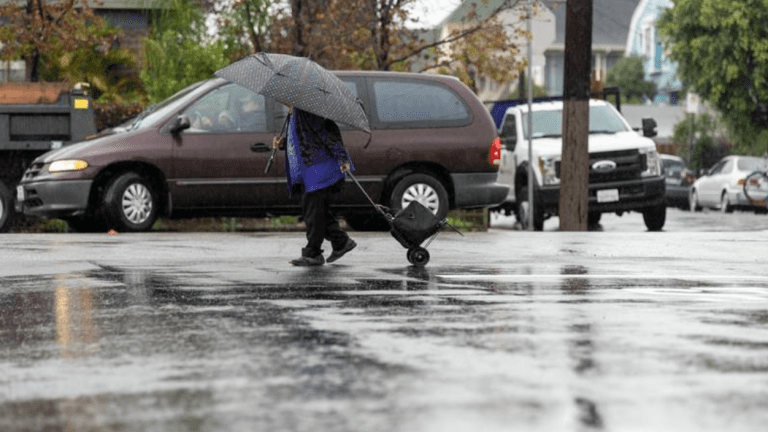 A lady who lives in the neighborhood of USC is walking in the rain.